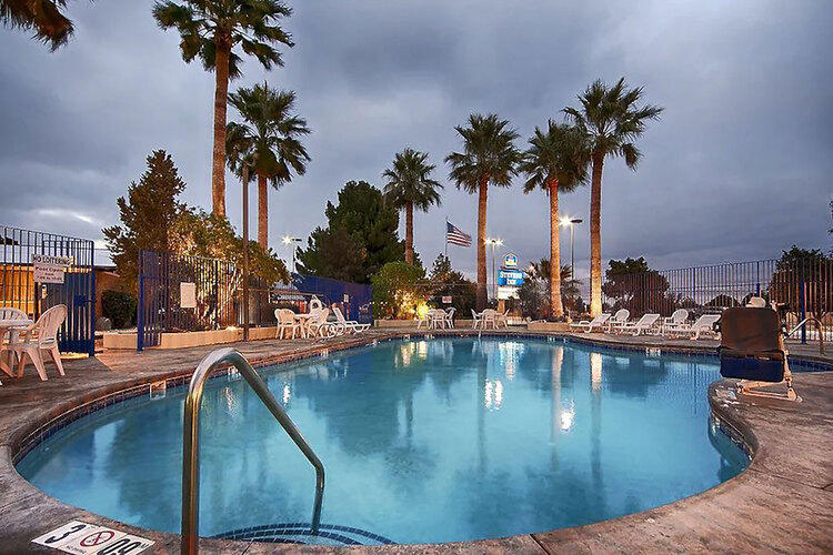 Outdoor pool surrounded by lounge chairs and palm trees in the evening